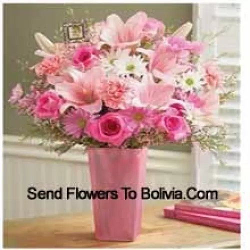Roses roses, oeillets roses, gerberas roses, gerberas blancs et lys roses avec des remplisseurs saisonniers dans un vase en verre